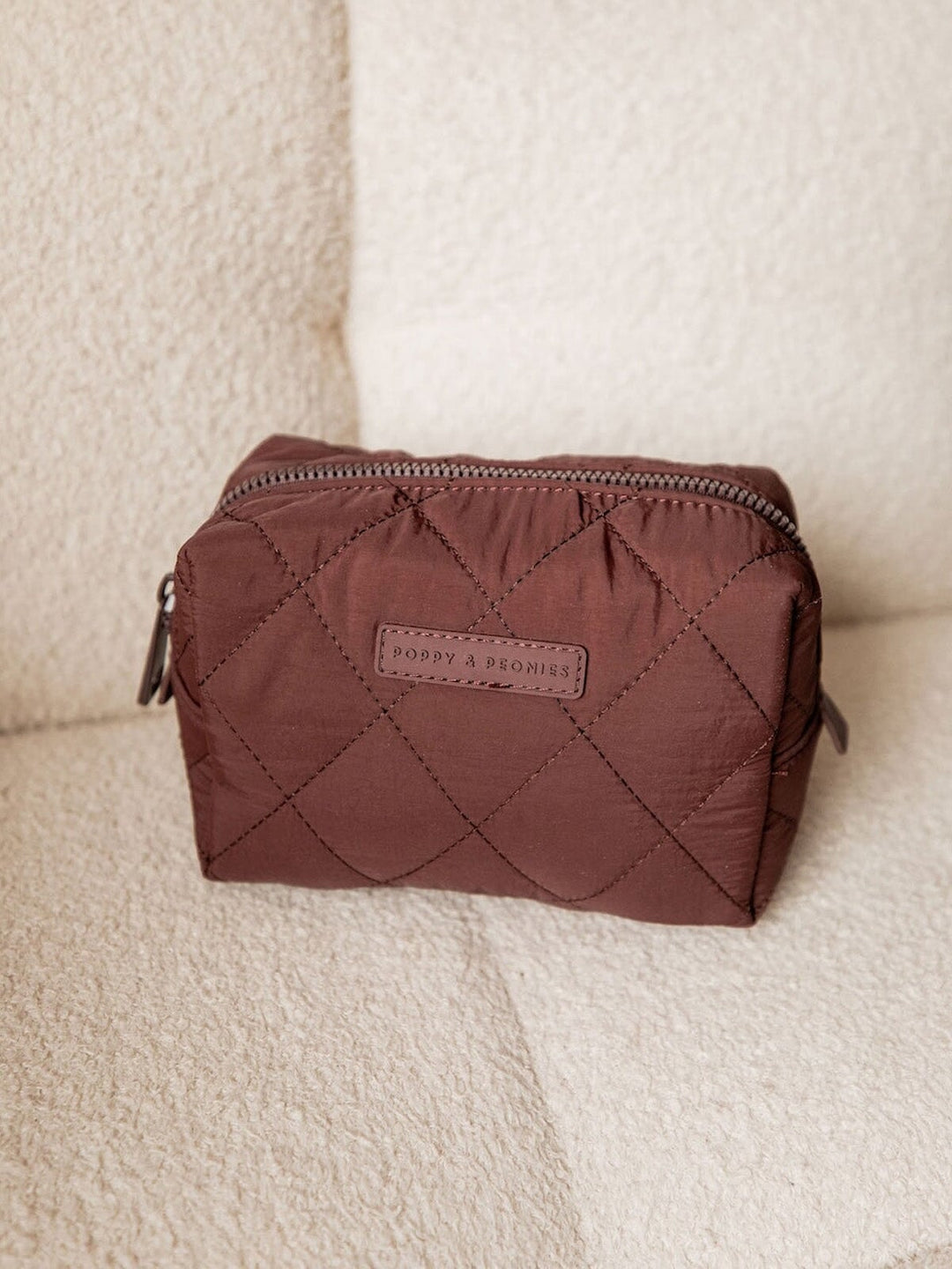 Quilted brown cosmetic bag with a brand label on a beige surface