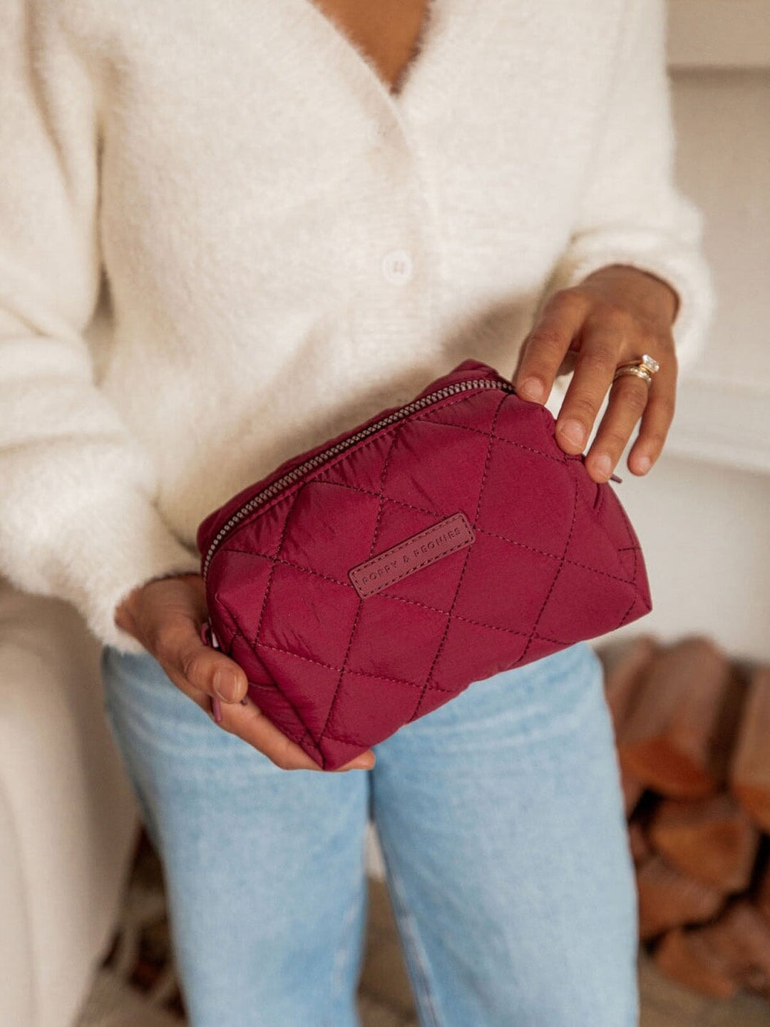 Person holding a berry coloured quilted makeup bag with a neutral background