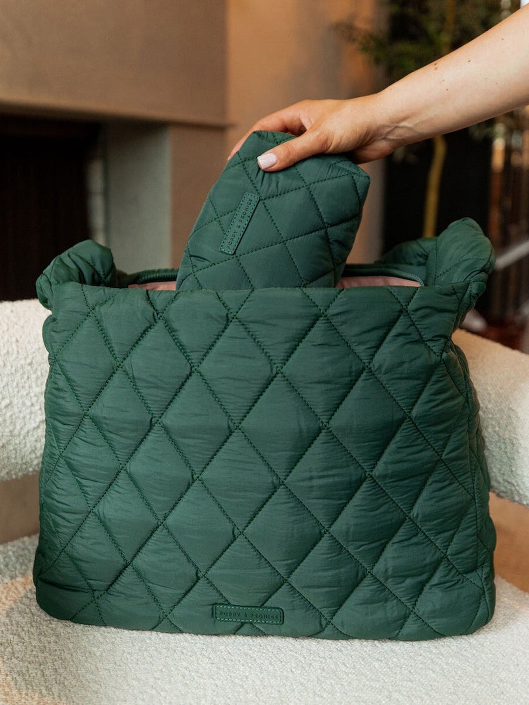 Person putting a green quilted makeup bag into a green quilted hobo bag