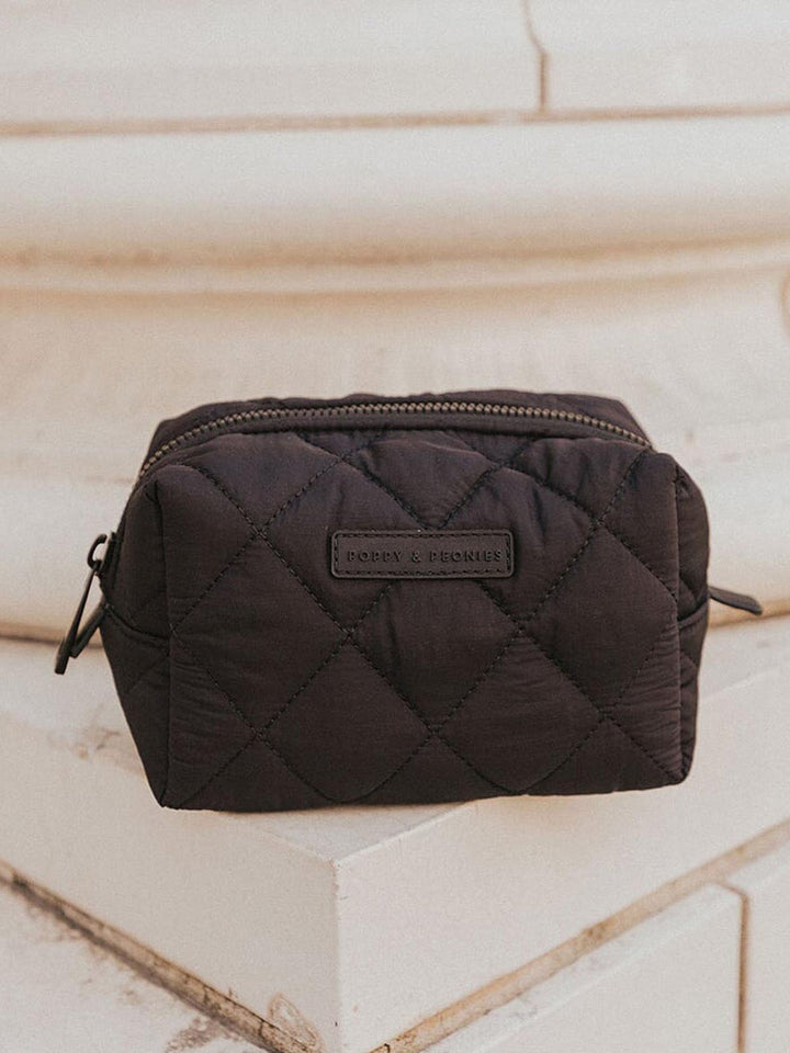 Black quilted cosmetic bag with a brand label on a light stone surface