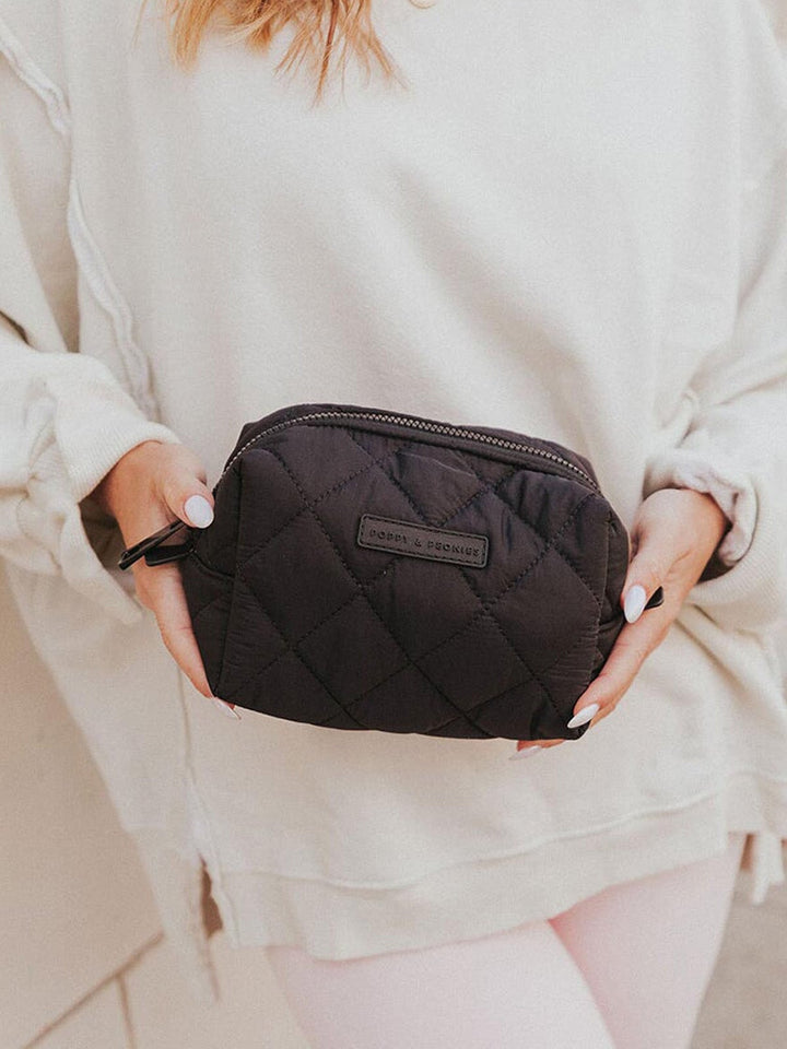 Person holding a black quilted makeup bag with a brand label.