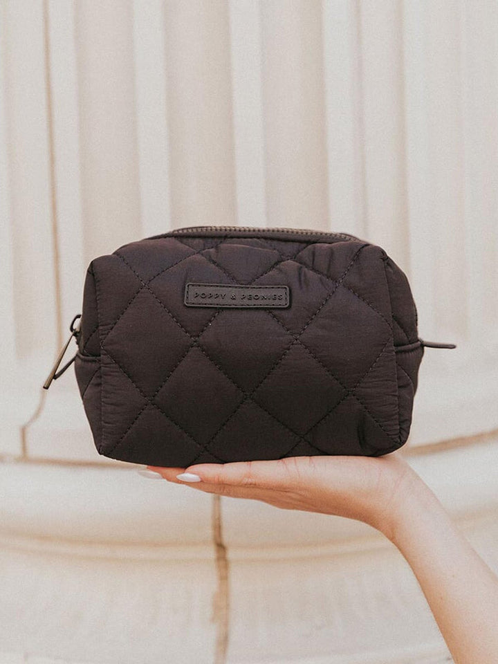 Black quilted cosmetic bag held by a hand against a neutral background