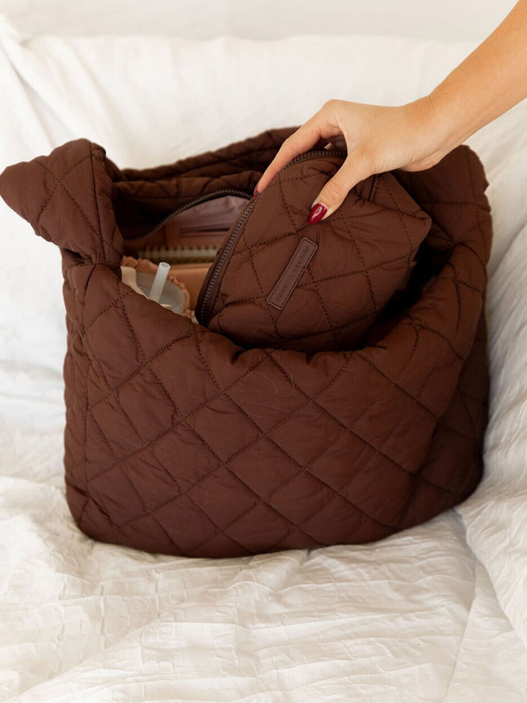 Brown quilted handbag with a hand reaching in to it