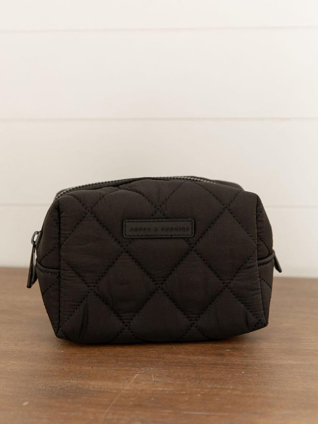 Black quilted cosmetic bag on a wooden surface with a white background