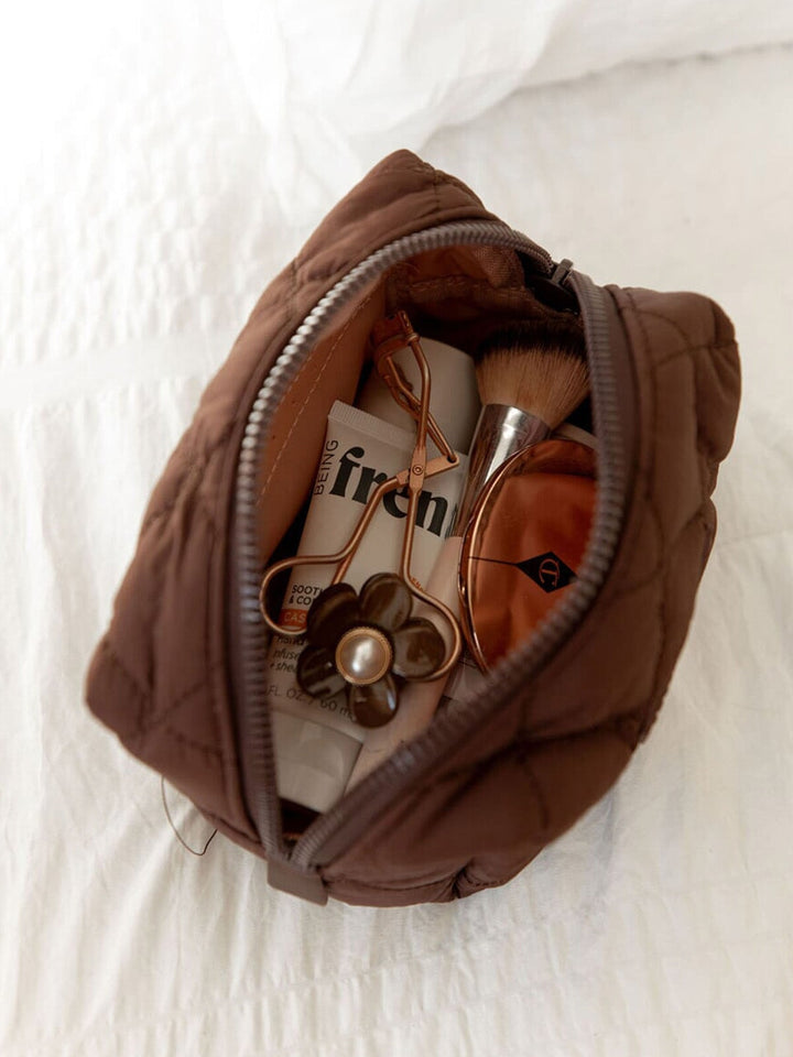 Brown quilted makeup bag with cosmetic items on a white background