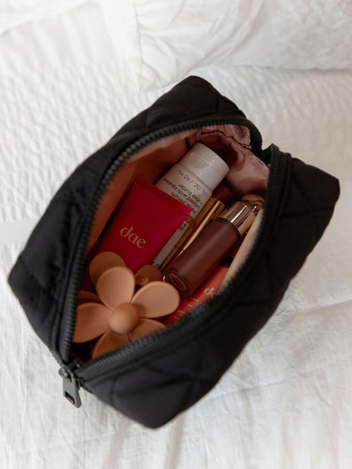 Black makeup bag with cosmetic items on a white textured surface