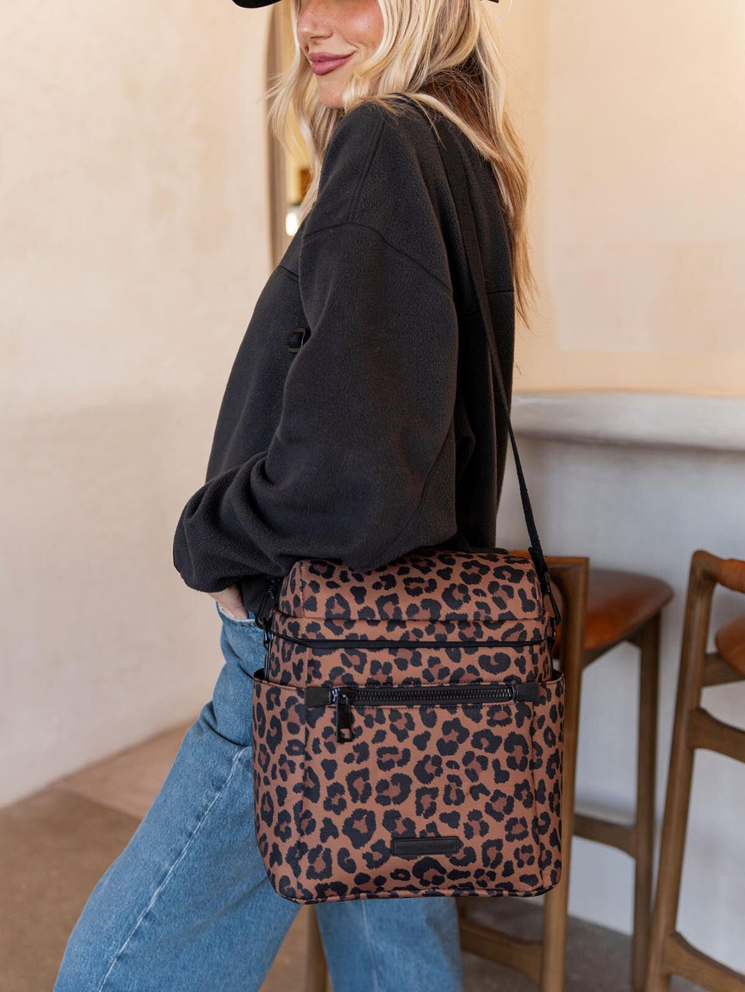 Person wearing a black sweatshirt and blue jeans with a leopard print lunch bag.