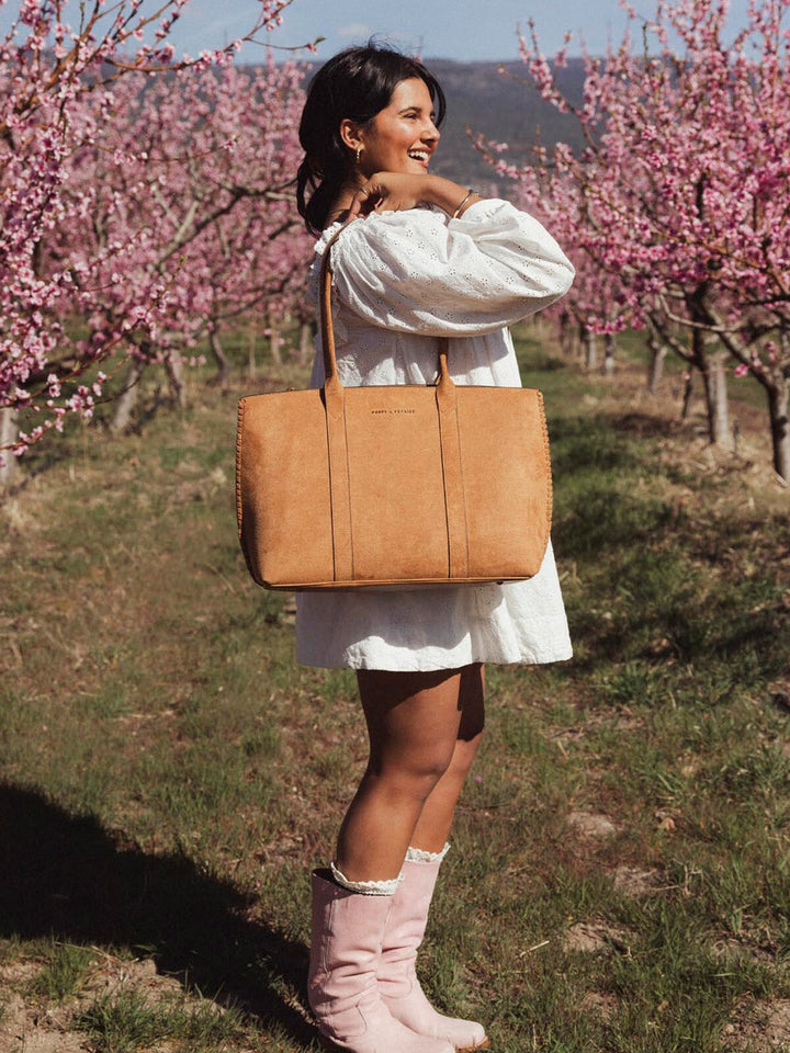 Woman in a white dress holding a brown vegan suede bag amongst cherry blossoms
