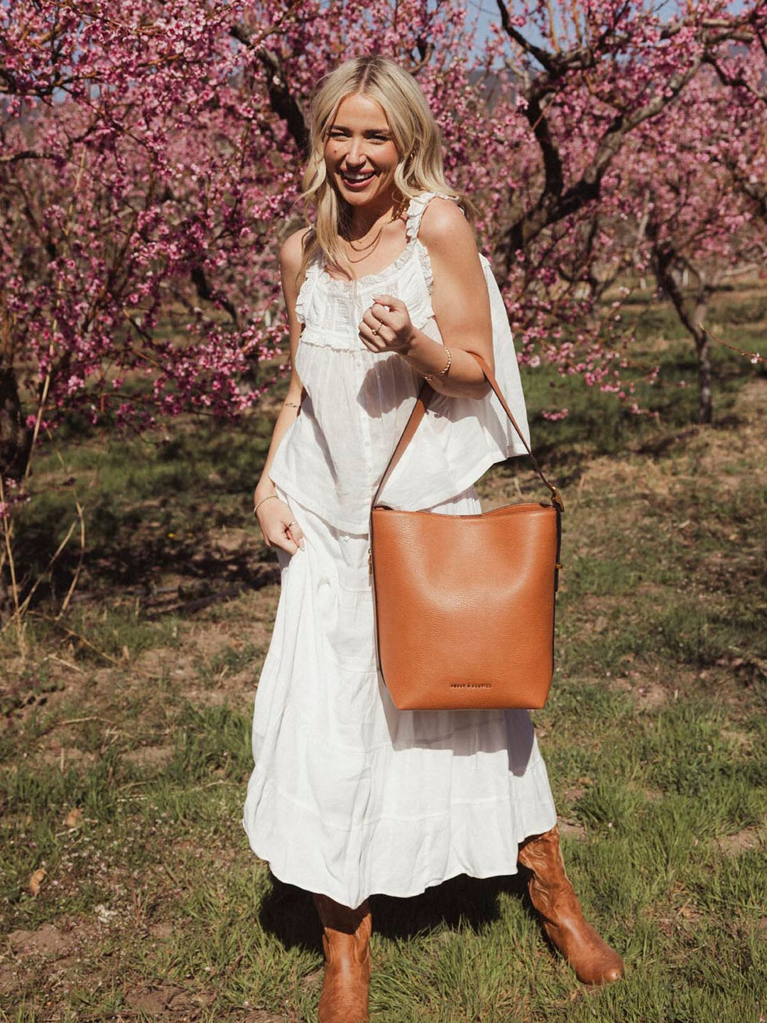 Woman holding a brown vegan leather bucket bag amongst cherry blossoms
