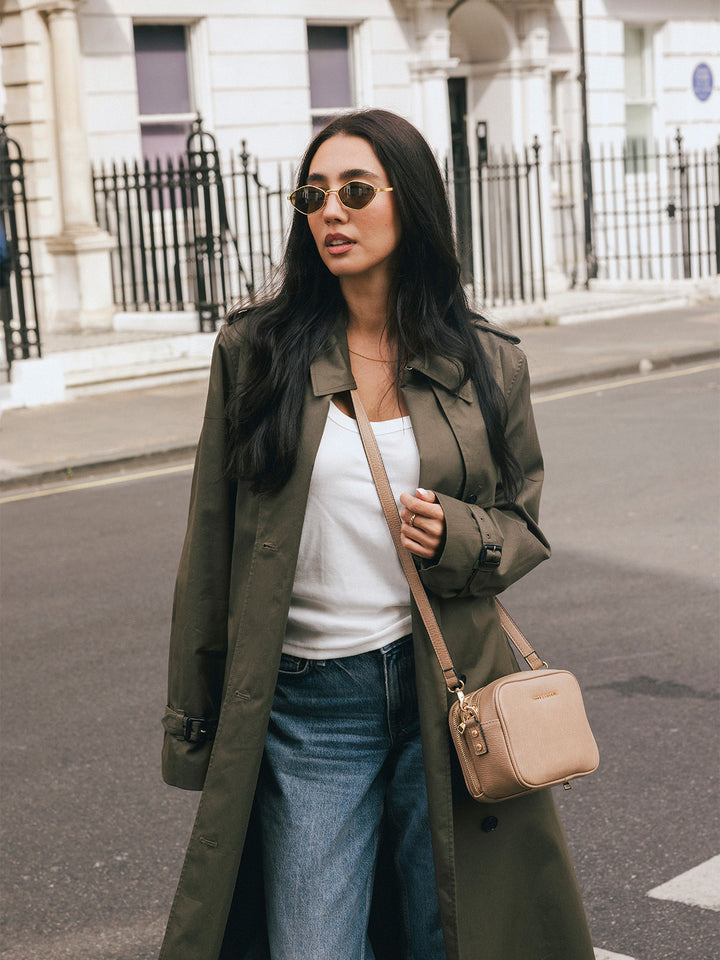 Woman wearing the Poppy & Peonies 24/7 Crossbody in Taupe at her side while standing on a city street.