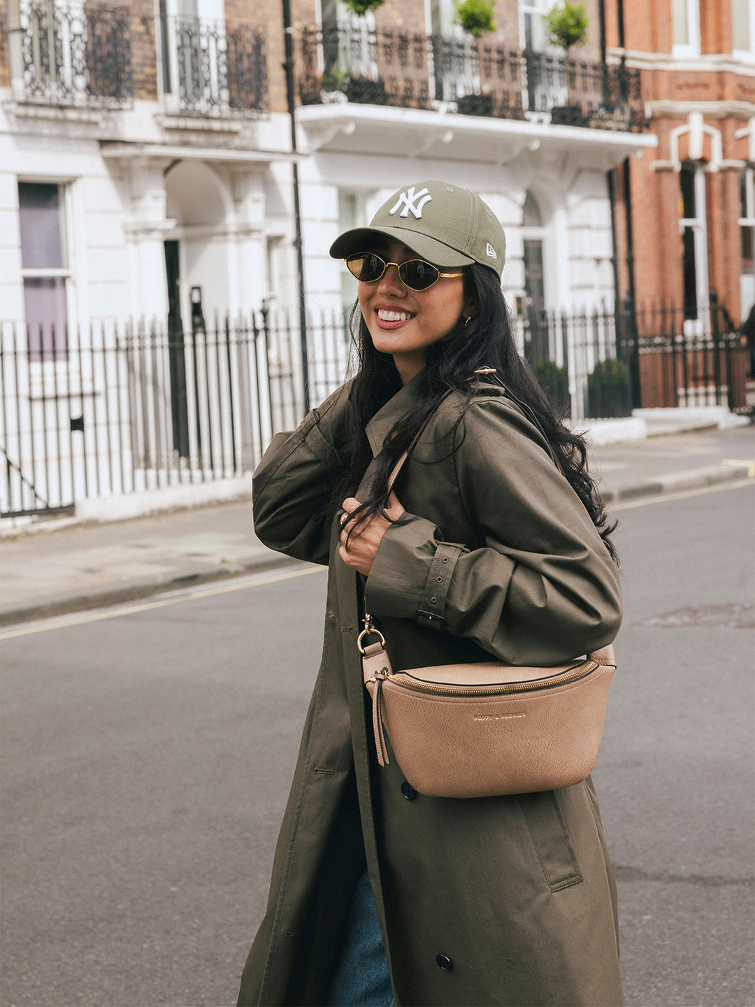 Woman wearing the Poppy & Peonies The Sidekick in Taupe at her hip while smiling on a city street.
