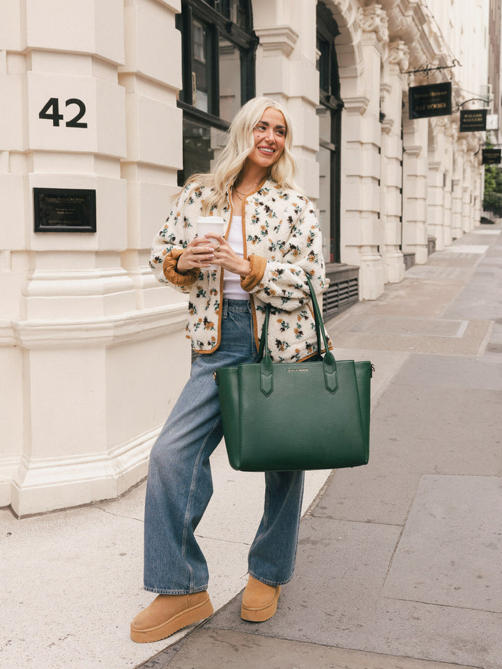 Woman carrying the Poppy & Peonies Double Duty Tote in Heritage Green by the top handles while walking through the city.