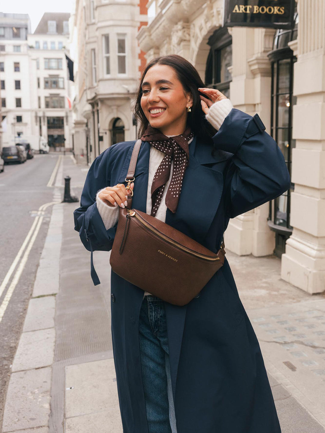 Lifestyle shot of a woman wearing the Poppy & Peonies Large Sidekick in Espresso crossbody while posing on a city street.