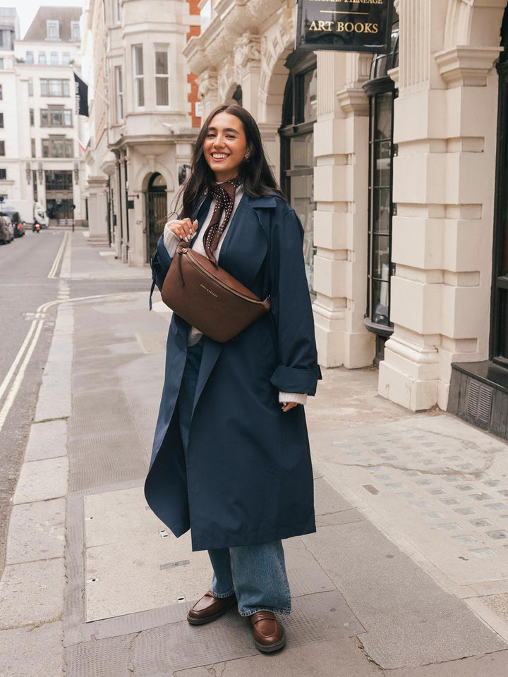 Full-body lifestyle shot of a woman wearing the Poppy & Peonies Large Sidekick in Espresso crossbody while walking along a city street.