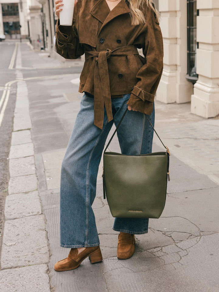 Product-focused lifestyle shot of the Poppy & Peonies Bucket Bag in Olive carried by the shoulder strap at the model’s side.