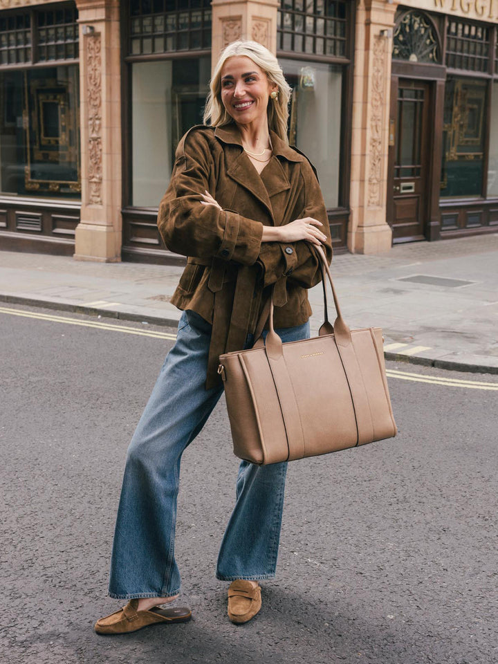 Woman posing with the Poppy & Peonies Multitasker in Taupe carried by the top handles on a city street.