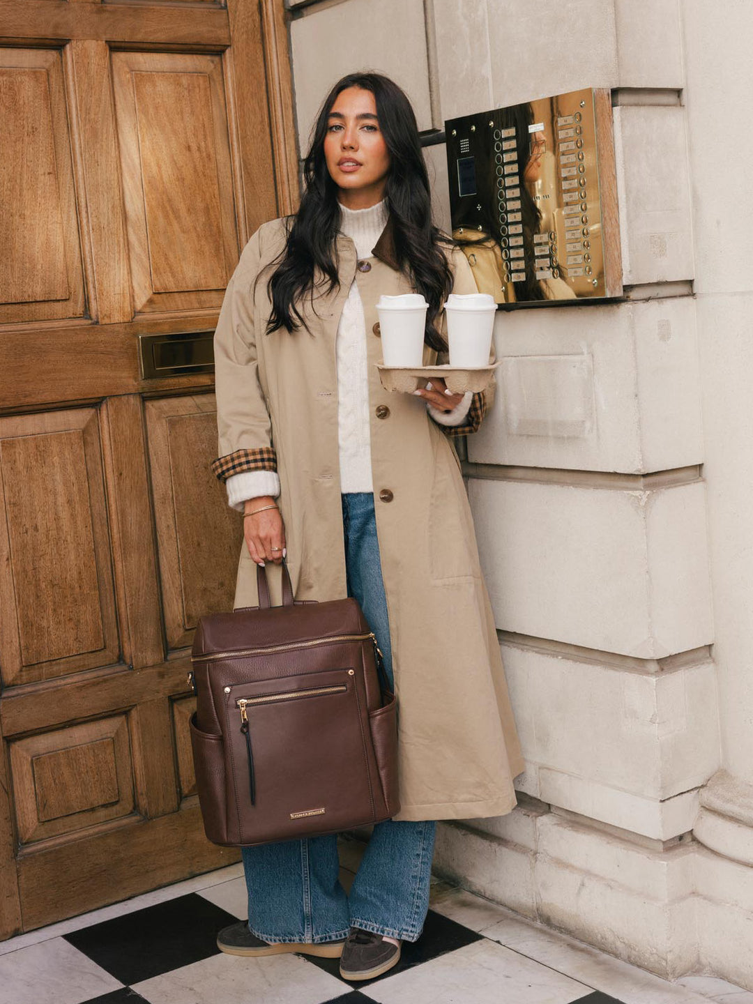 Woman carrying the Poppy & Peonies Commuter Backpack in Espresso by the top handle while holding takeaway cups.