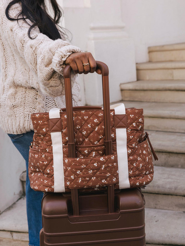 Close-up of the Poppy & Peonies Mini Voyager in Brown Floral secured to the handle of a rolling suitcase.