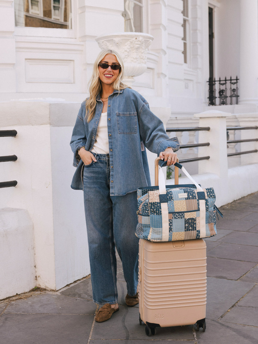 Woman posing with the Poppy & Peonies Mini Voyager in Navy Patchwork secured over the handle of a rolling suitcase.