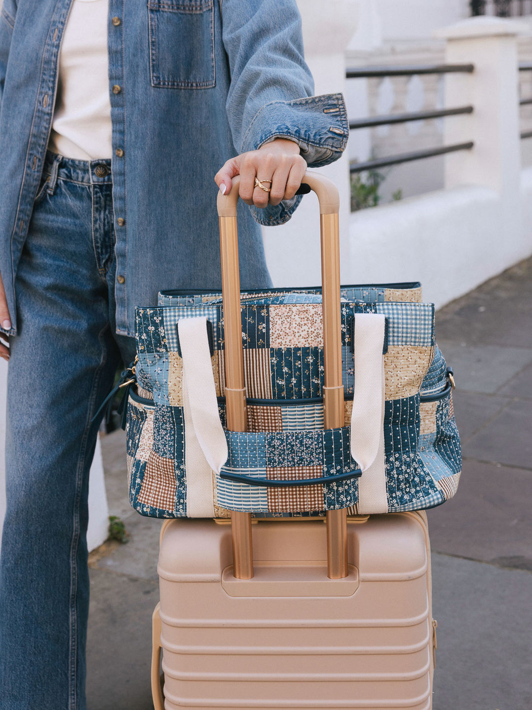 Close-up of the Poppy & Peonies Mini Voyager in Navy Patchwork secured over the handle of a rolling suitcase.
