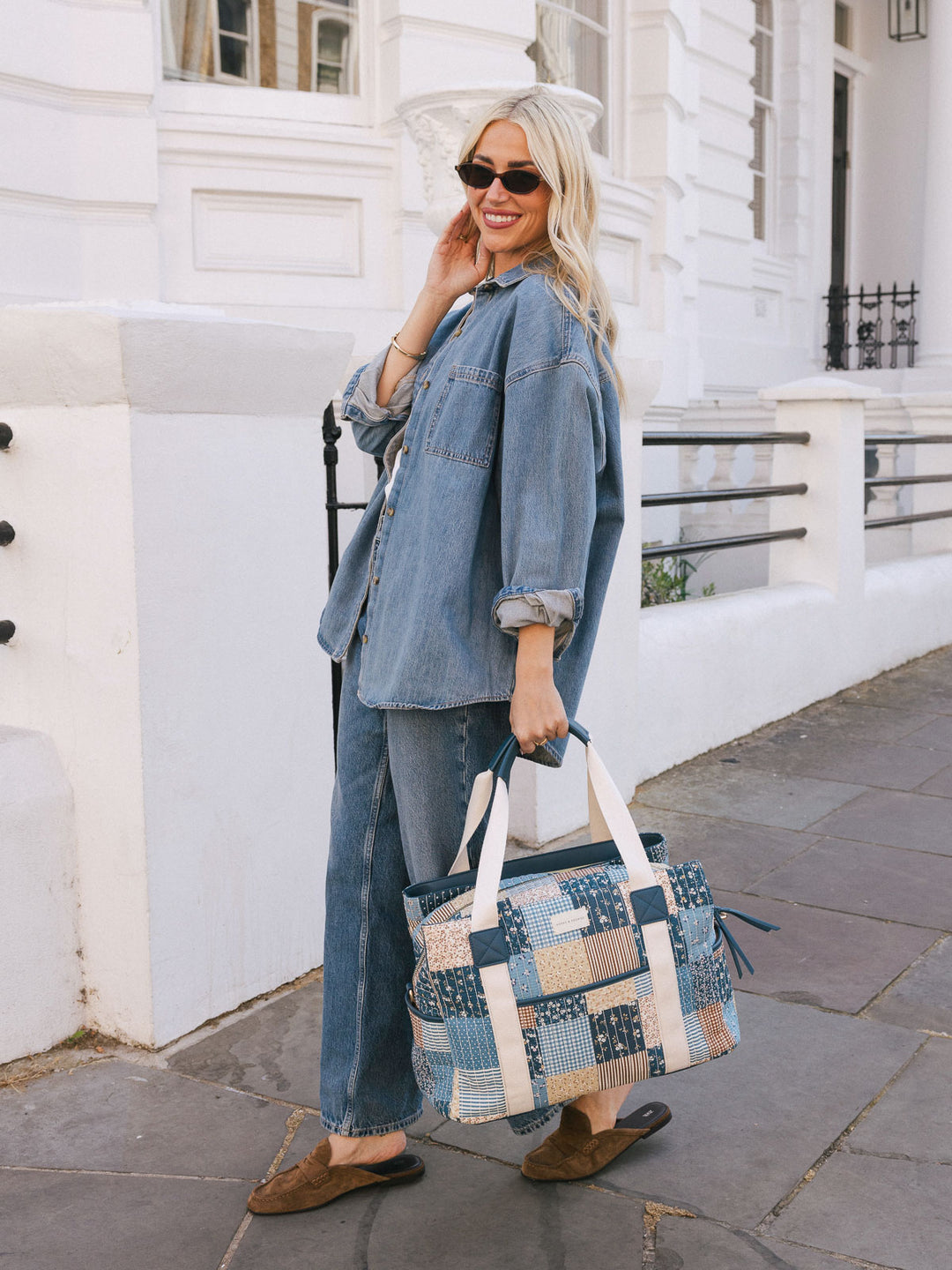 Woman carrying the Poppy & Peonies Mini Voyager in Navy Patchwork by the top handles while walking outdoors.