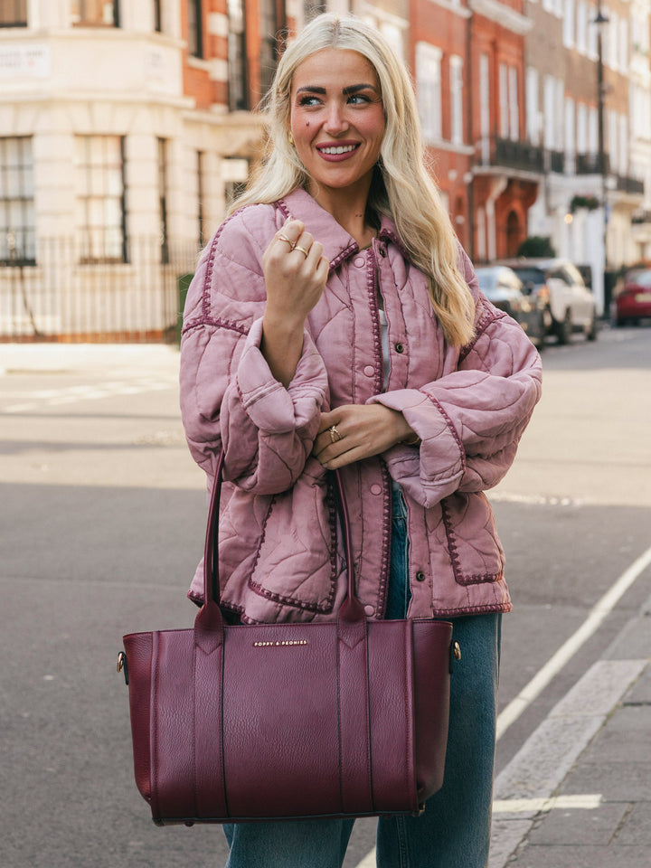 Woman holding the Poppy & Peonies Small Multitasker in Berry by the top handles while smiling on a city street.