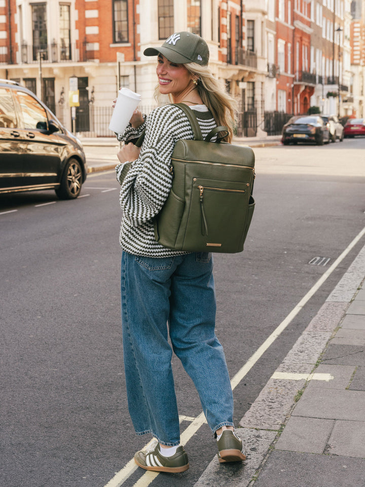 Woman wearing the Poppy & Peonies Commuter Backpack in Olive on her back while walking along a city street