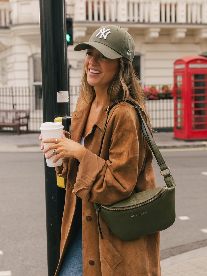 Woman carrying the Poppy & Peonies Sidekick in Olive over her shoulder while holding a takeaway coffee on a city street.