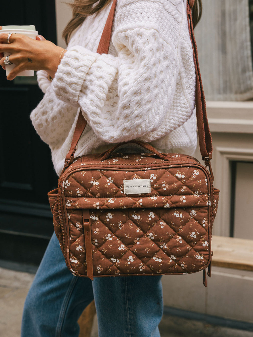 Close-up product-focused shot of the Poppy & Peonies Basic Lunch Bag in Brown Floral worn over the shoulder, highlighting the quilted floral print, top handle, front pocket, and adjustable shoulder strap.