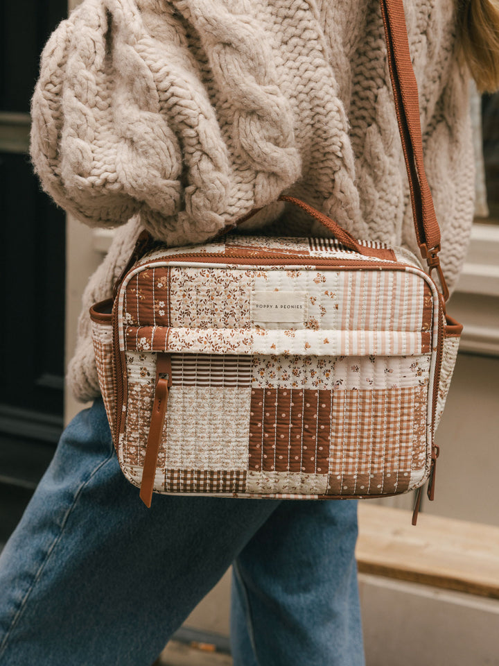 Close-up product-focused shot of the Poppy & Peonies Basic Lunch Bag in Brown Patchwork worn over the shoulder, highlighting the patchwork print and front pocket.
