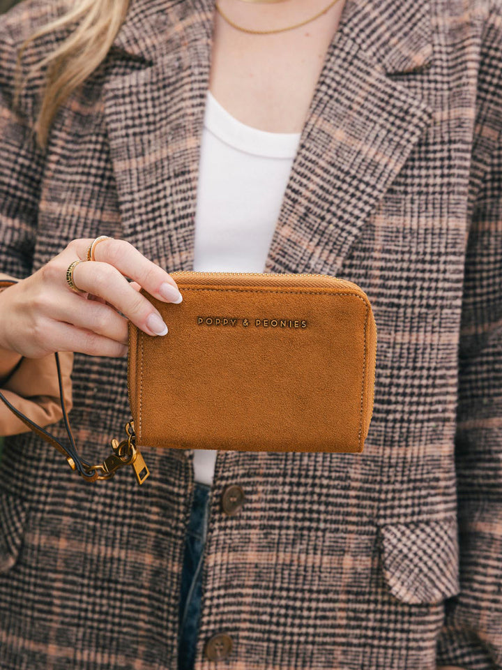 Poppy & Peonies The Grab and Go Wallet in Cognac Suede held in hand outdoors, showing its compact silhouette and gold-tone logo.