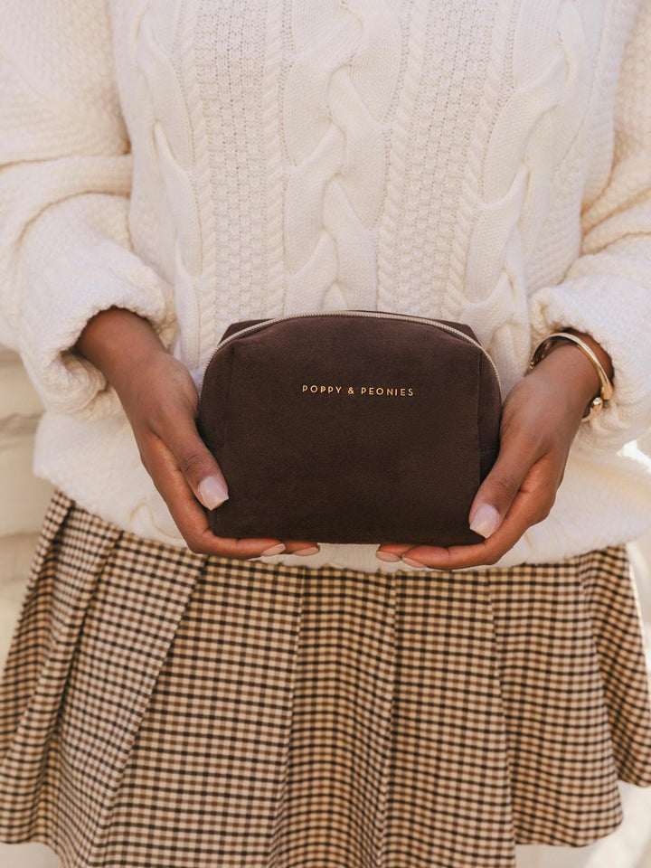 Poppy & Peonies Cosmetic Case in Espresso Suede held with both hands, showing its compact size, rounded shape and gold-tone logo.