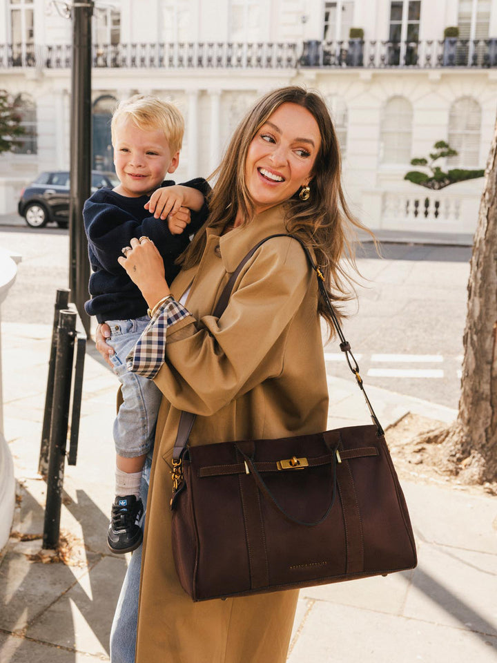 Poppy & Peonies Effortless Tote in Espresso Suede carried while holding a child outdoors, showcasing its spacious silhouette and front belting detail.