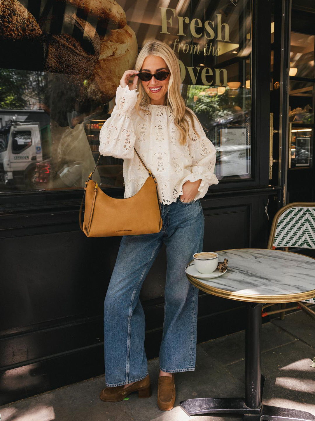 Poppy & Peonies The Sunday Bag in Cognac Suede worn over the shoulder outside a café, styled with a white eyelet blouse and jeans.