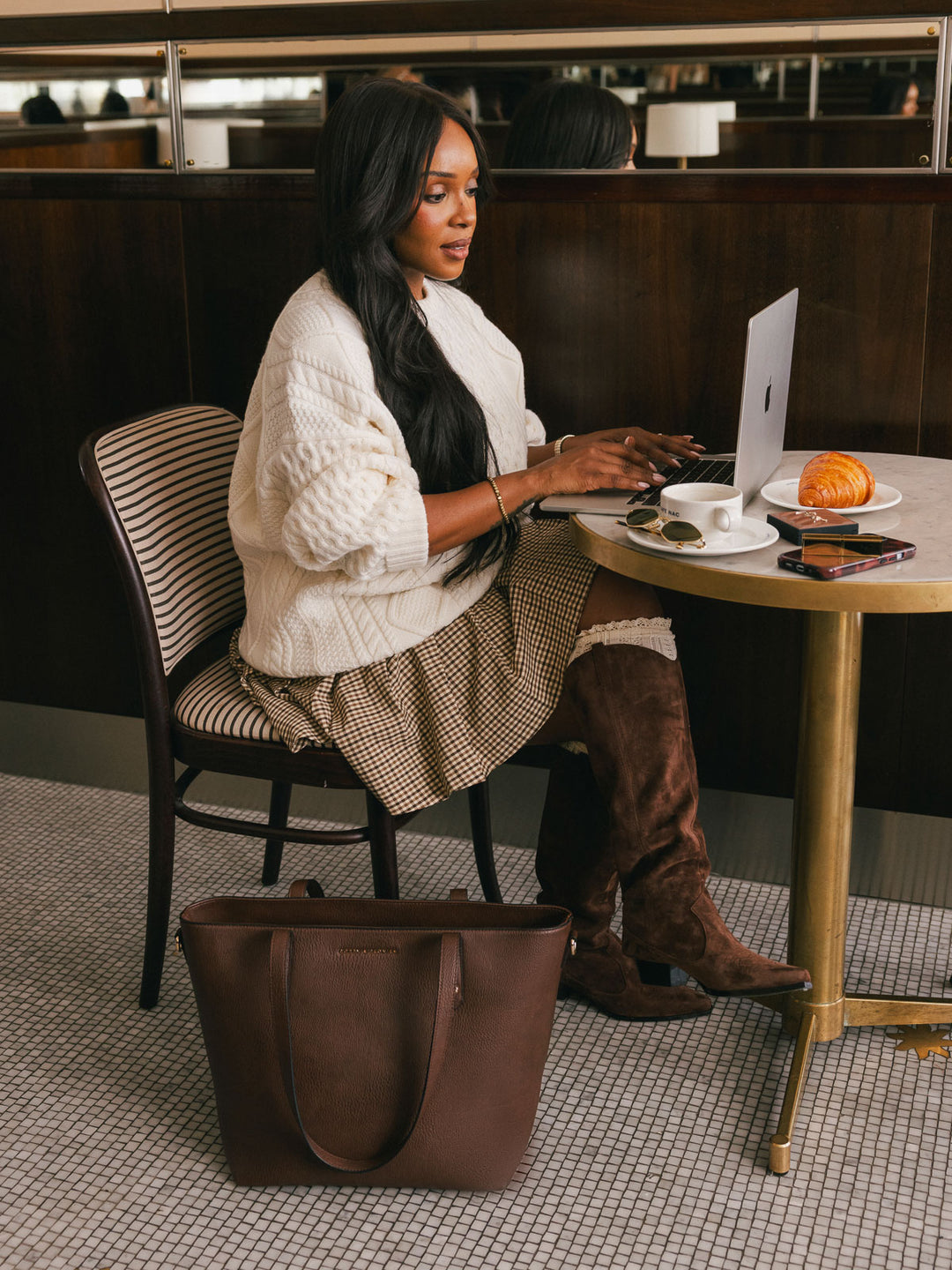 Seated lifestyle shot of a woman working on a laptop with the Poppy & Peonies Go-Getter Tote in Espresso displayed beside her.