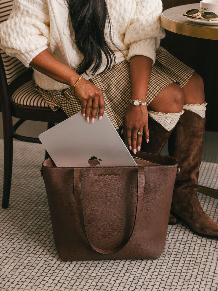 Close-up lifestyle shot of a woman placing a laptop inside the Poppy & Peonies Go-Getter Tote in Espresso, highlighting its spacious interior.