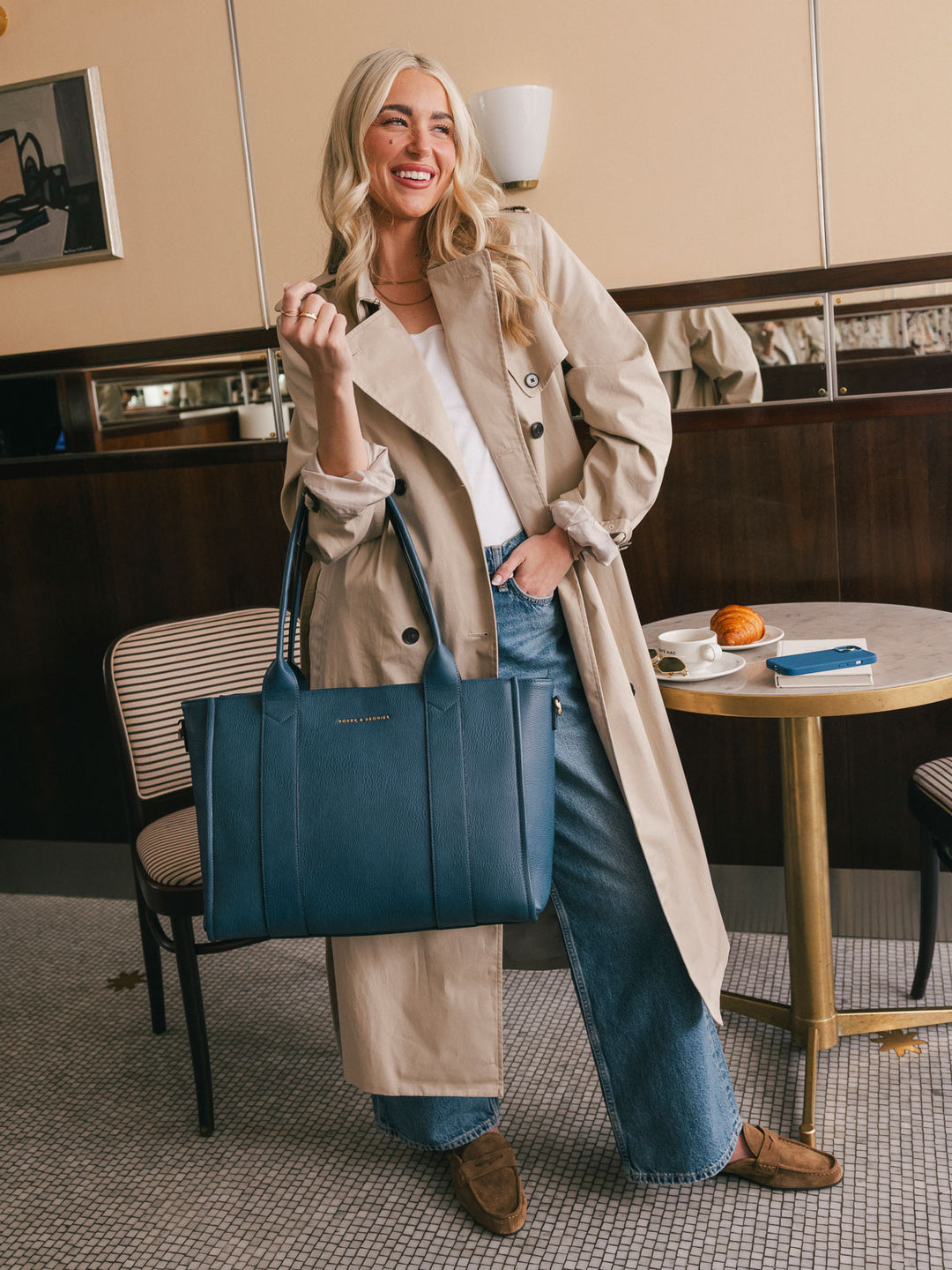 Full-body lifestyle shot of a woman carrying the Poppy & Peonies Multitasker in Navy over her shoulder beside a café table.