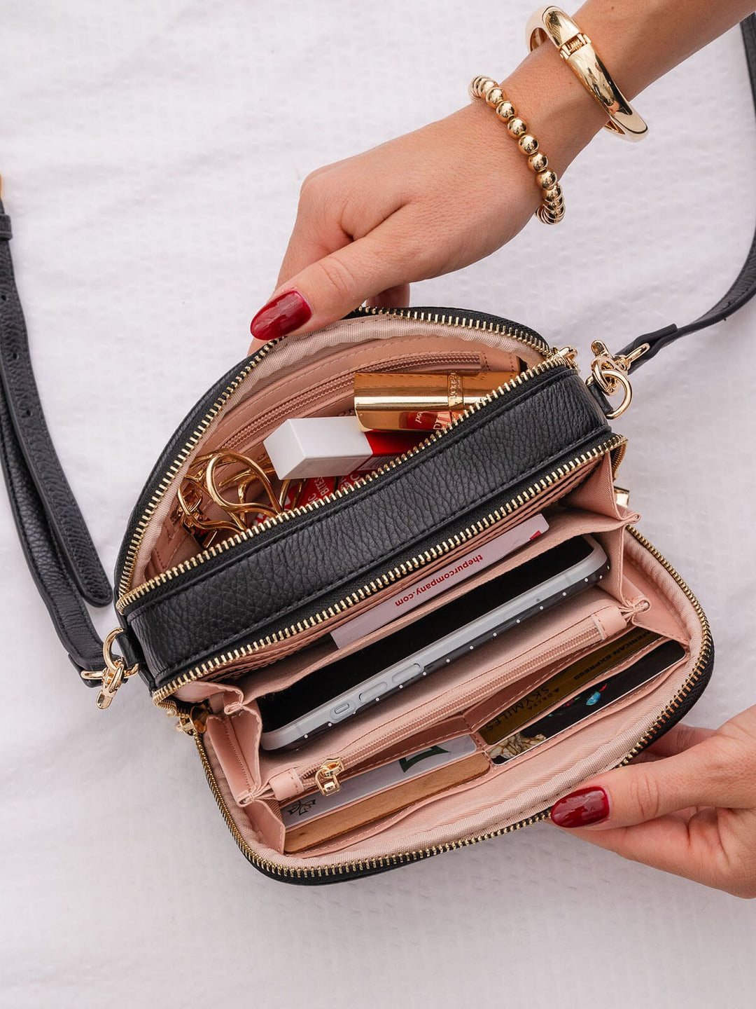 Black handbag with gold accents open on a white background, showing its contents.