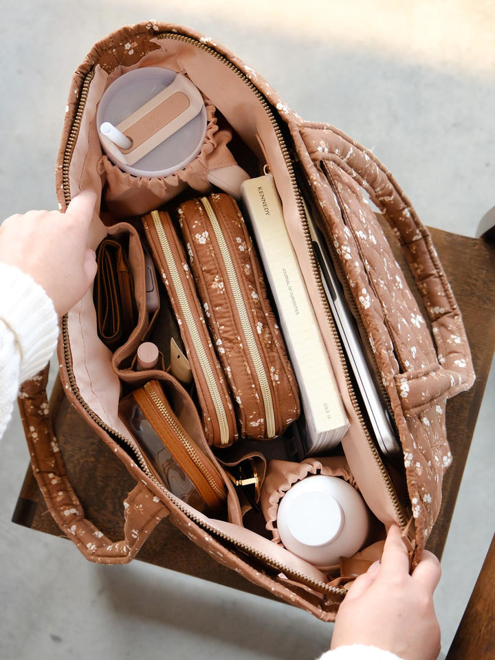 Overhead view of the Daydreamer Tote in Brown Floral showcasing its organized interior filled with cosmetic cases, a wallet, books, drink bottle, and other daily essentials.