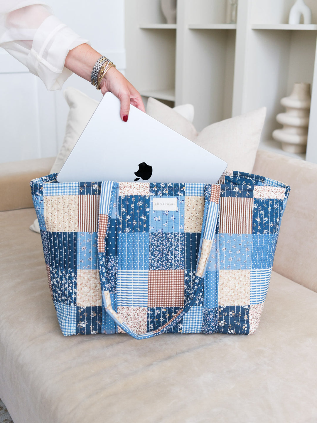 Lifestyle shot of the Daydreamer Tote in Navy Patchwork with a laptop being placed inside, highlighting its spacious design and structured top handles.