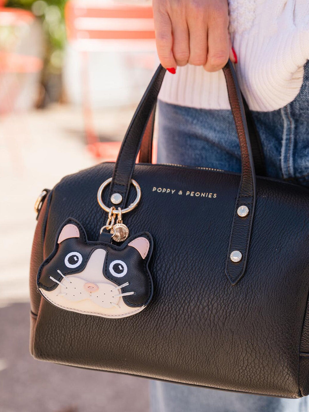 Black handbag with a cat-shaped bag charm held by a person.