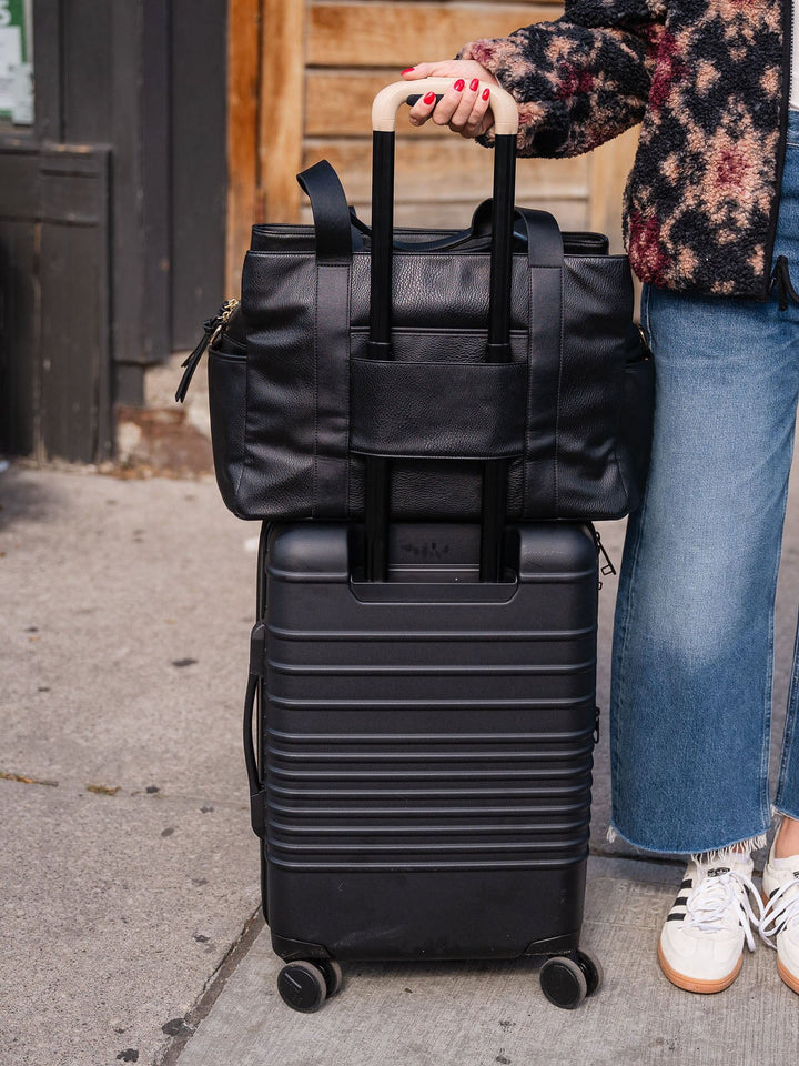 Close-up of the Poppy & Peonies Mini Voyager in Black secured over the handle of a rolling suitcase.