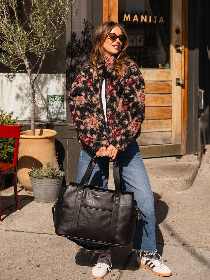 Woman carrying the Poppy & Peonies Mini Voyager in Black while posing outdoors.
