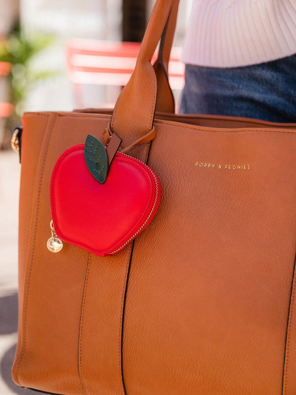 Brown tote bag with a red apple-shaped coin pouch bag charm attached.