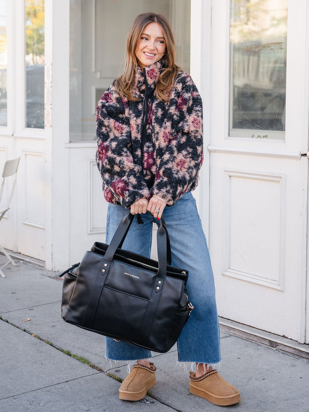 Woman holding the Poppy & Peonies Mini Voyager in Black by the top handles while posing on a city 