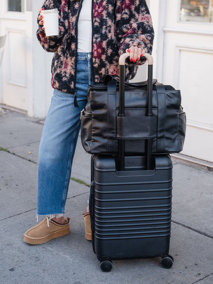 Close-up of the Poppy & Peonies Mini Voyager in Black secured over the handle of a rolling suitcase.