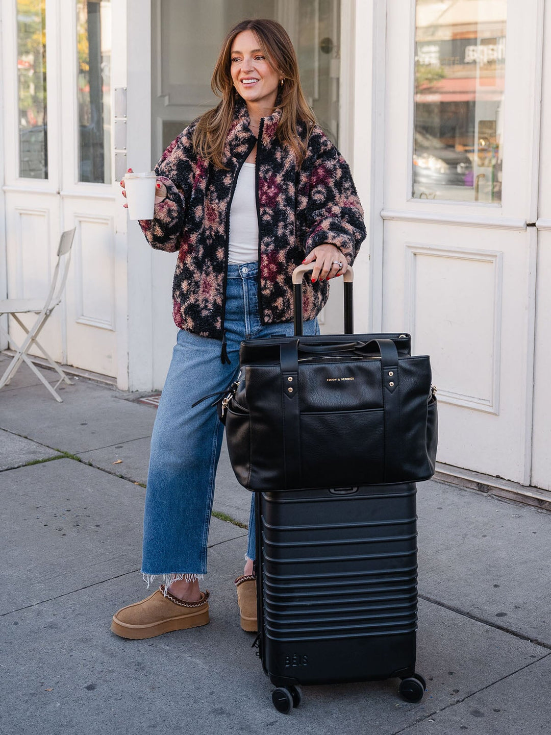 Woman posing with the Poppy & Peonies Mini Voyager in Black secured over the handle of a rolling suitcase.