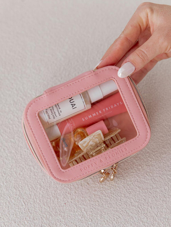 Pink cosmetic bag with beauty products inside, held by a hand on a light background