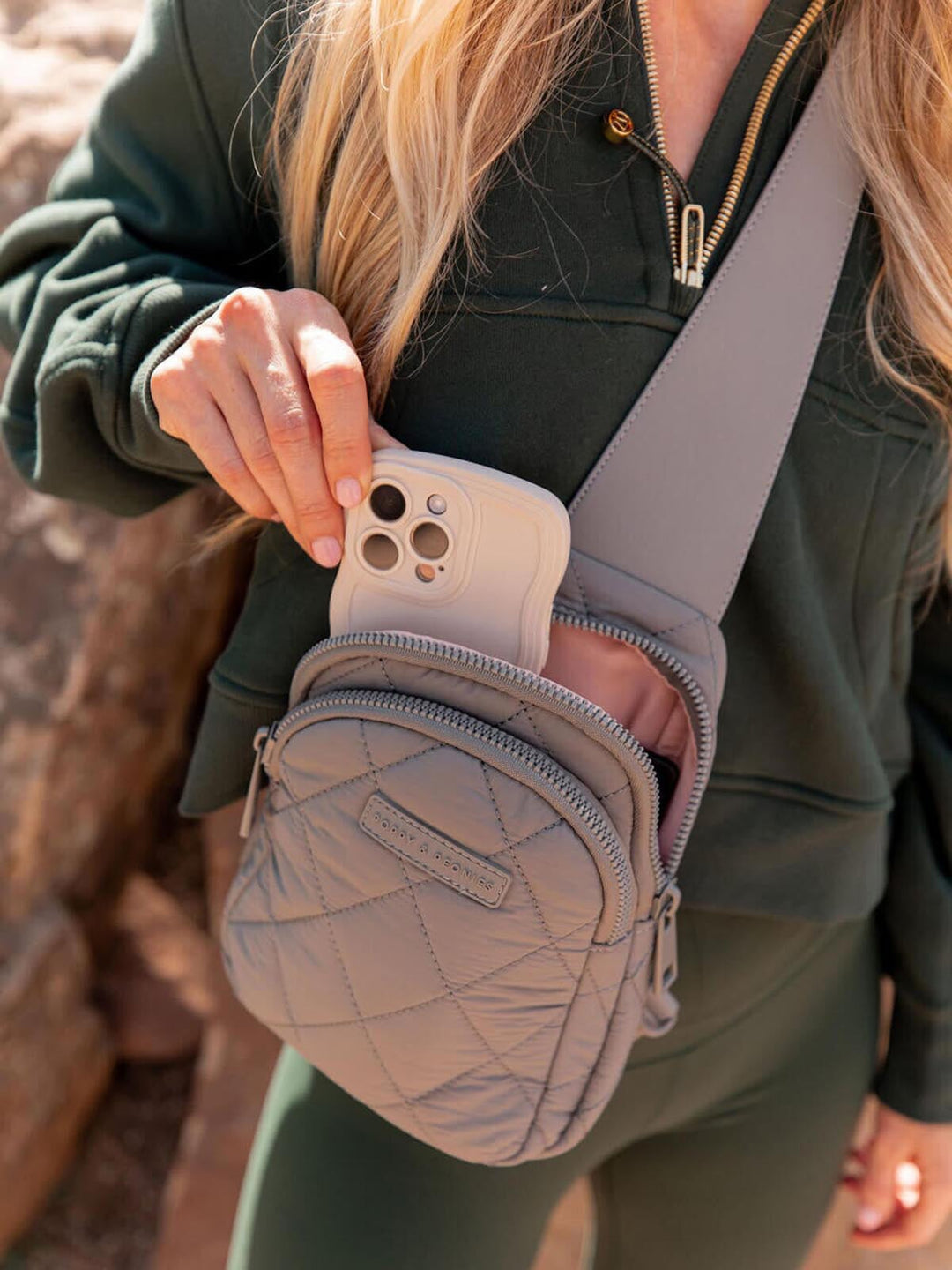 Person holding a phone case with a quilted grey crossbody bag on a natural background