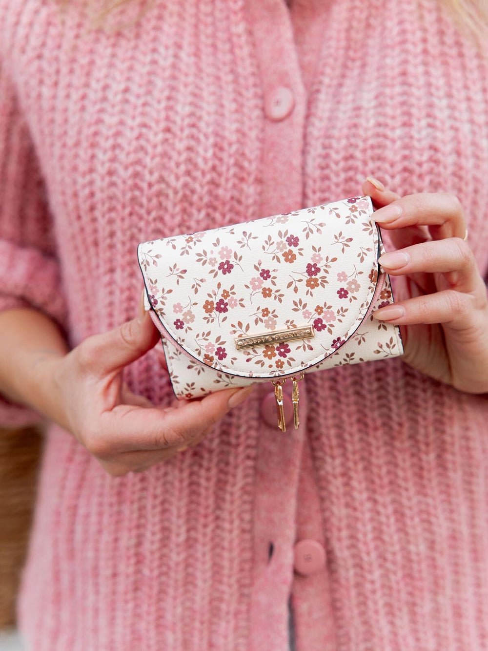 Floral-patterned wallet held by a person wearing a pink textured cardigan.